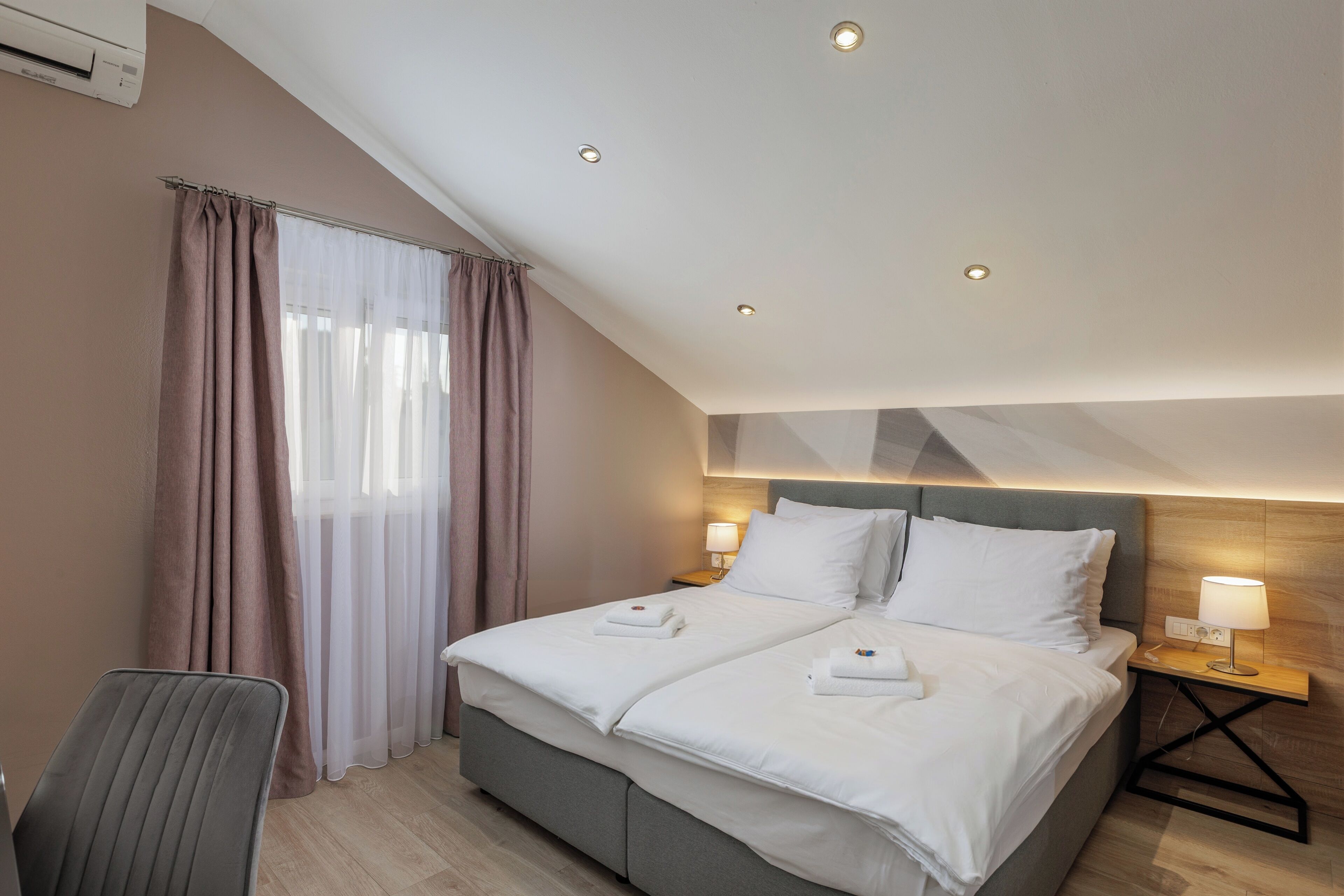 A hotel room with a bed, two bedside lamps, a chair, and a window with curtains.