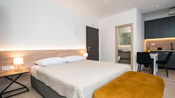 A modern hotel room with a bed, bedside table, lamp, and a small desk area with a chair.