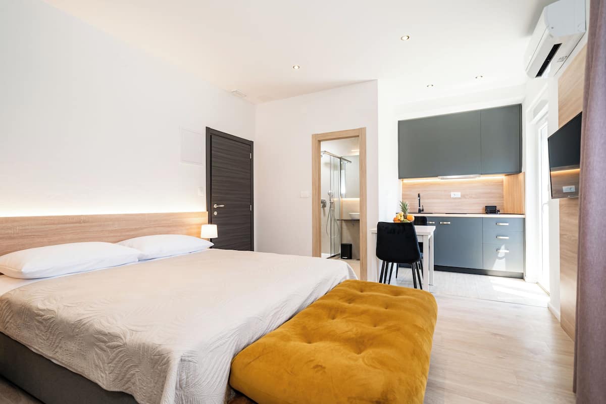 Un dormitorio moderno con una cama grande, un escritorio pequeño y una kitchenette al fondo.