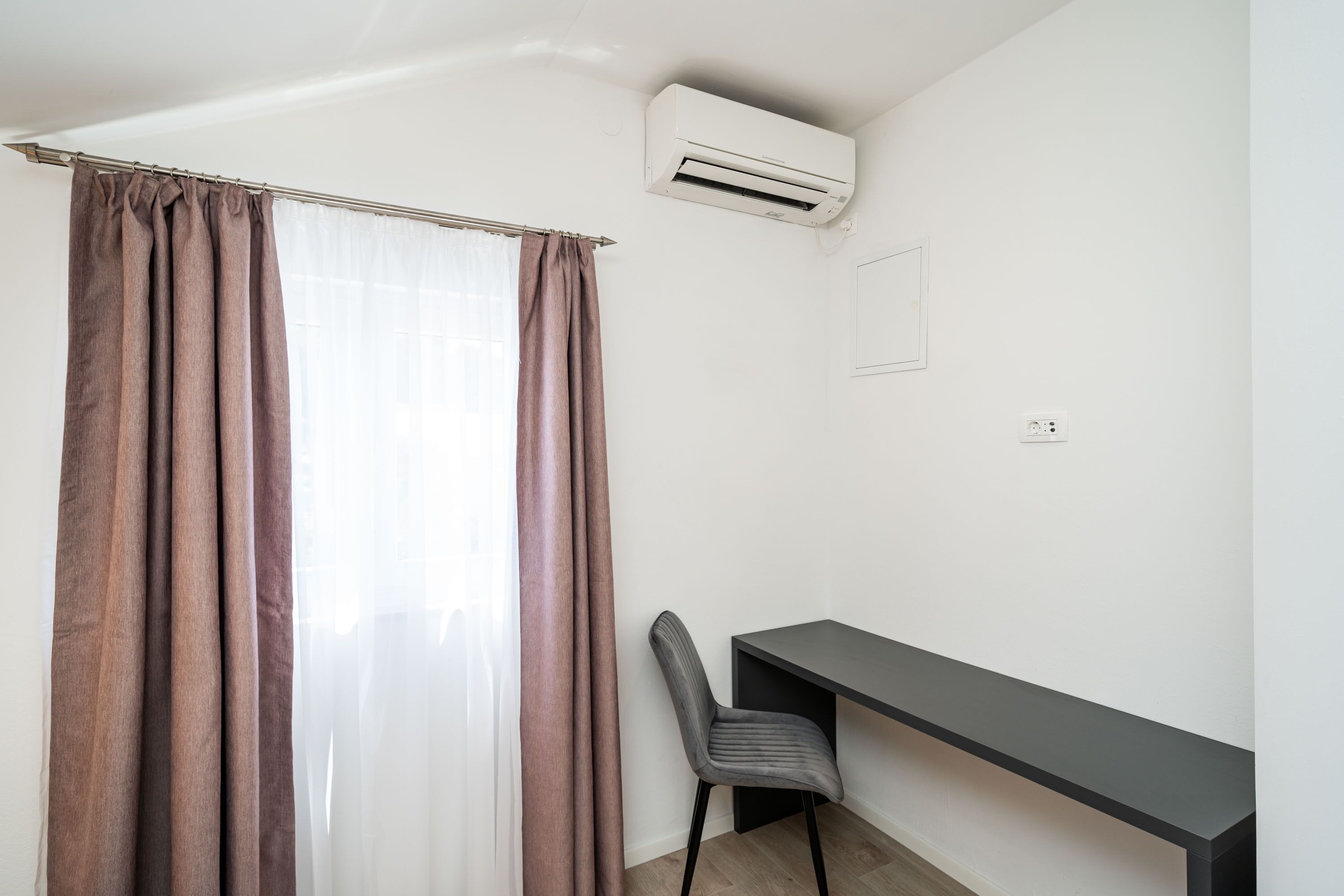 A room with a desk, chair, and an air conditioning unit.
