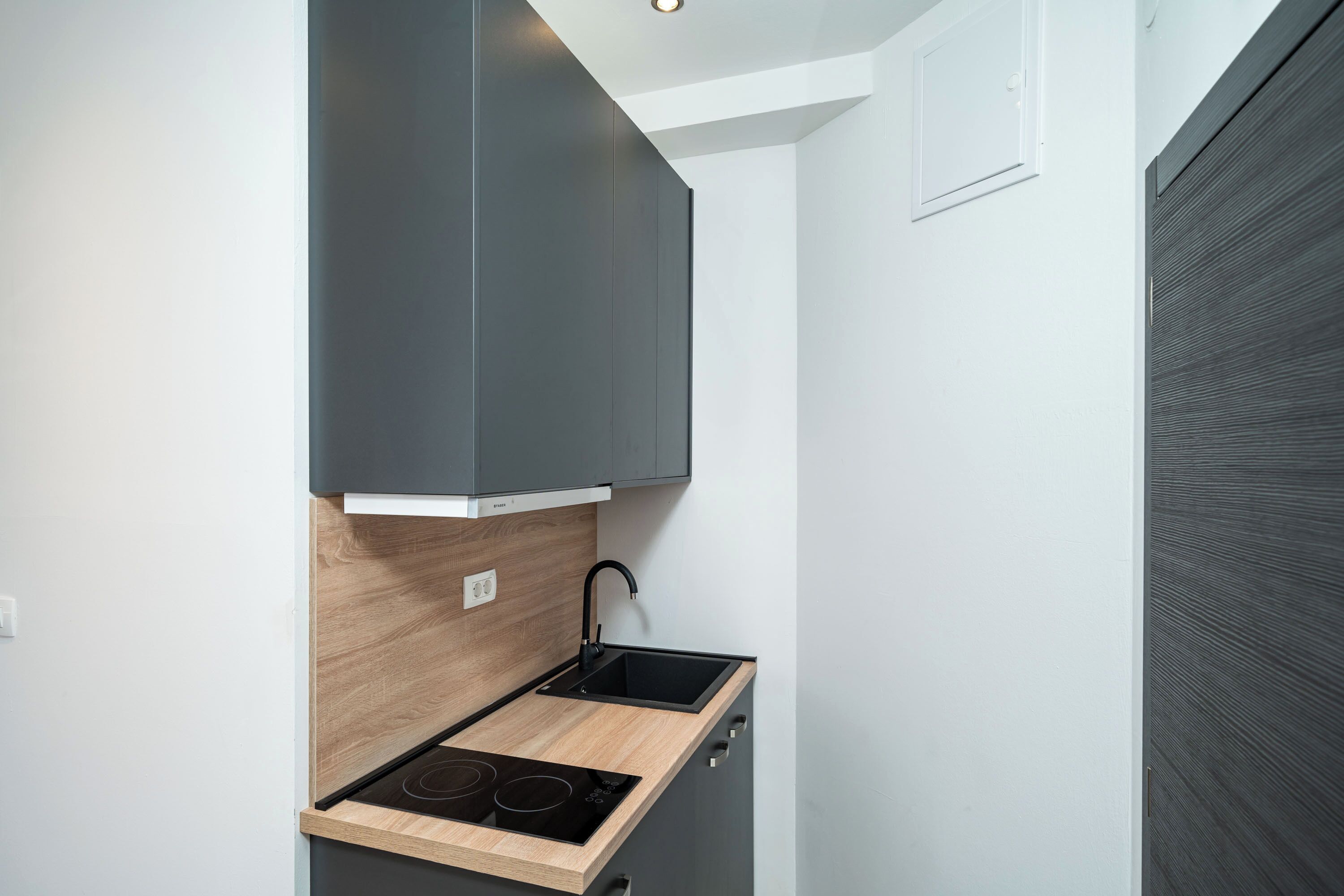 Eine kompakte Küche mit modernem Design, ausgestattet mit einem eingebauten Gaskochfeld, einem schwarzen Spülbecken und dunklen Schränken.
