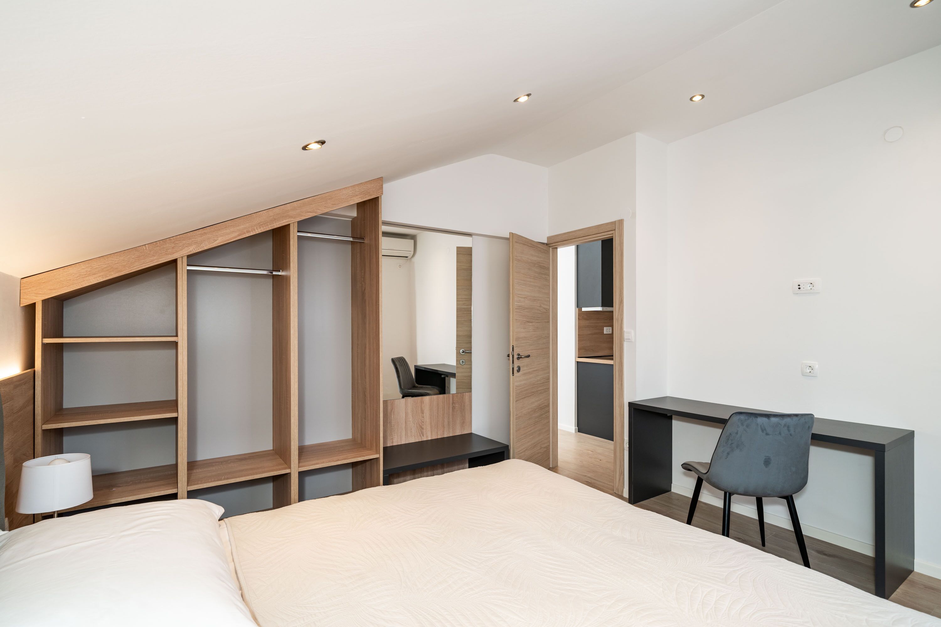 A bedroom with a bed, a desk, a chair, and built-in shelving.