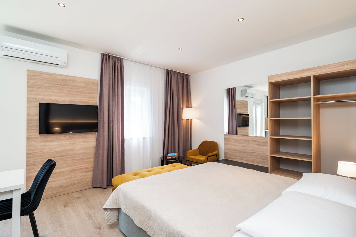 Una habitación de hotel con cama, televisión, silla, lámpara y armario.