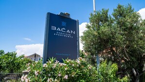 Cartel de BACAN Service Apartments, con cielo despejado y vegetación al fondo.