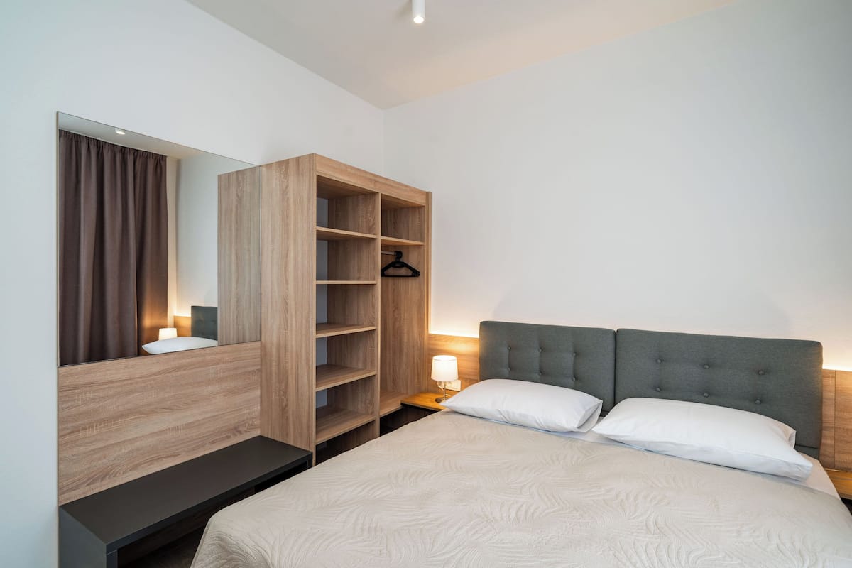 Una habitación de hotel con una cama grande, un armario de madera, una mesita de noche con lámpara y un espejo.