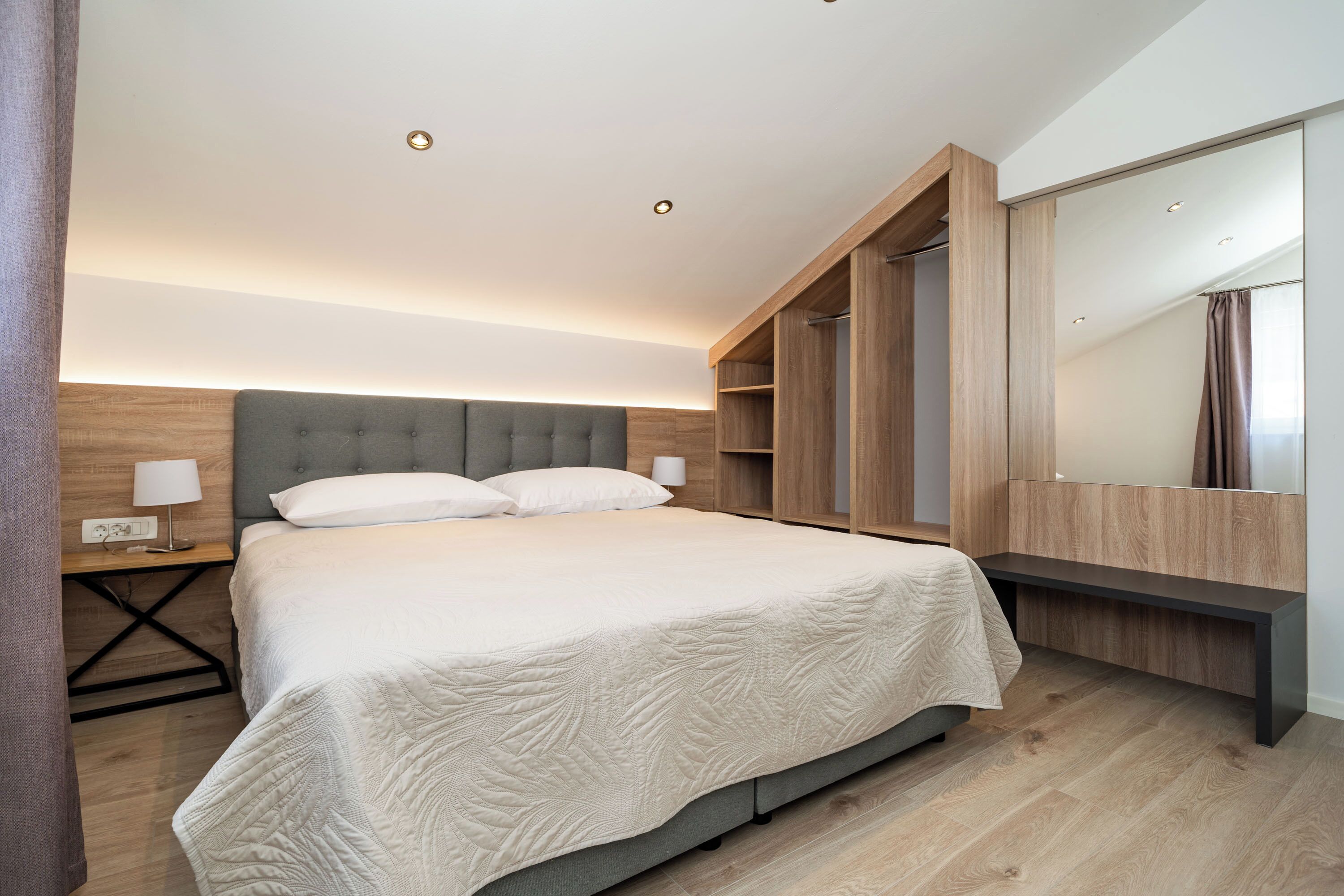 A modern bedroom with a large bed, bedside tables, a wardrobe, and a mirror.