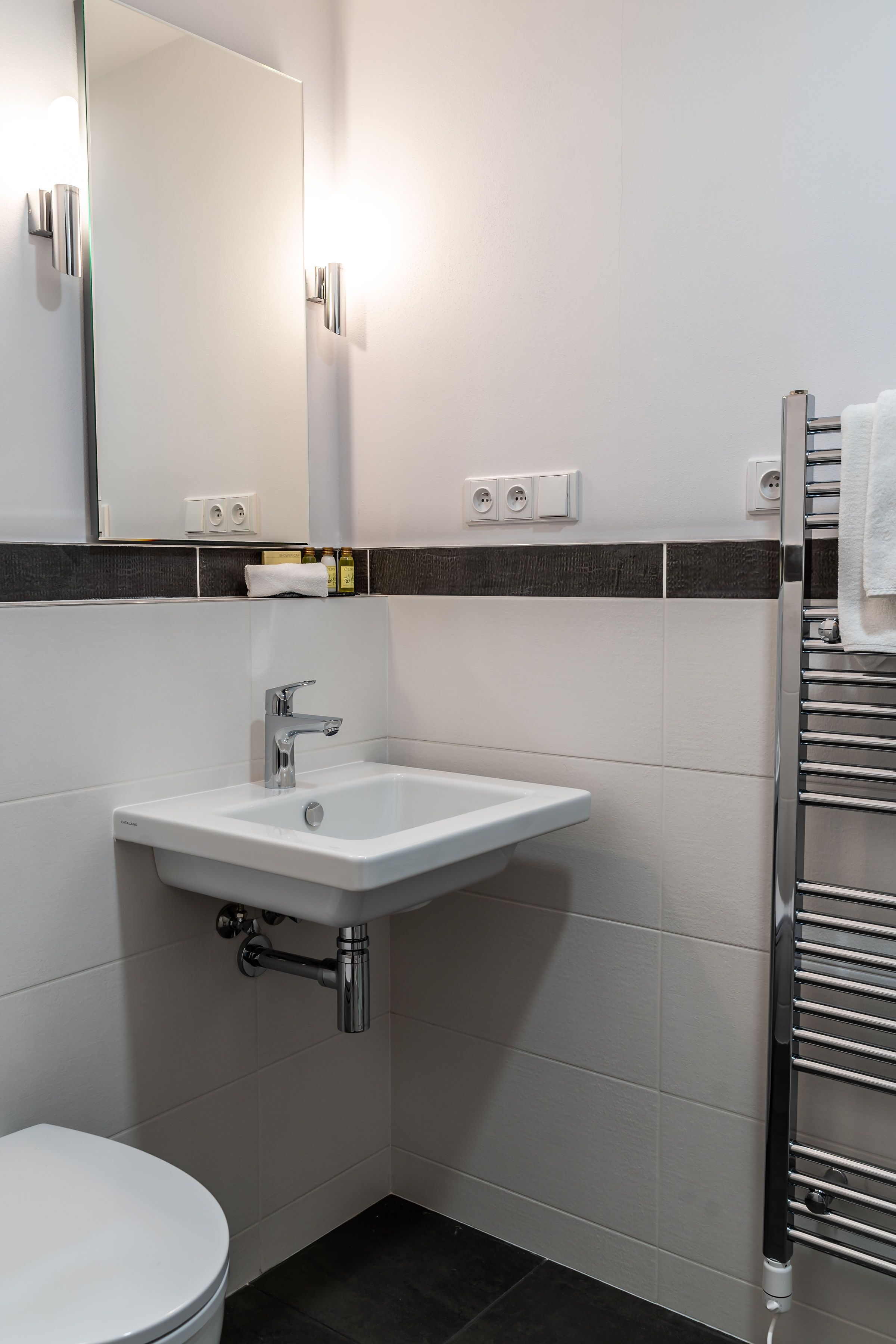 Een moderne badkamer met een wit wastafelmeubel, een spiegel, een handdoekhouder en een toilet.