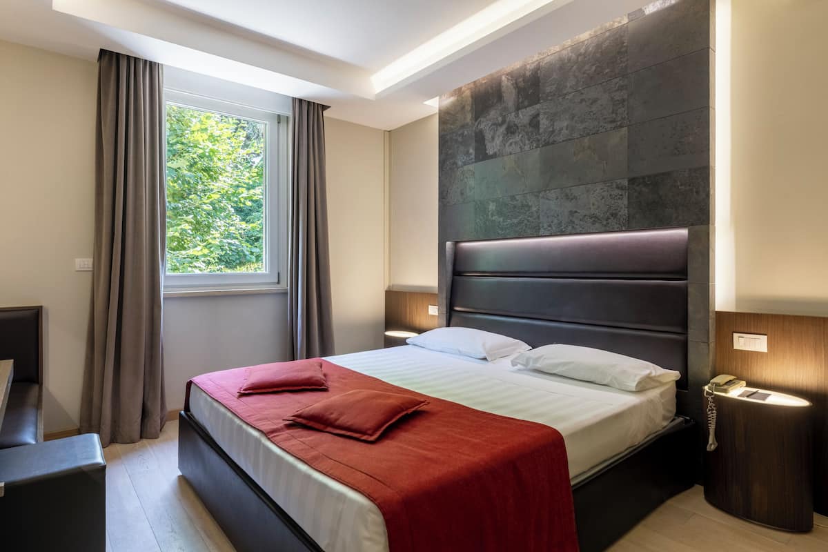 Una habitació d'hotel moderna amb un llit gran, una taula de nit i una finestra amb cortines.