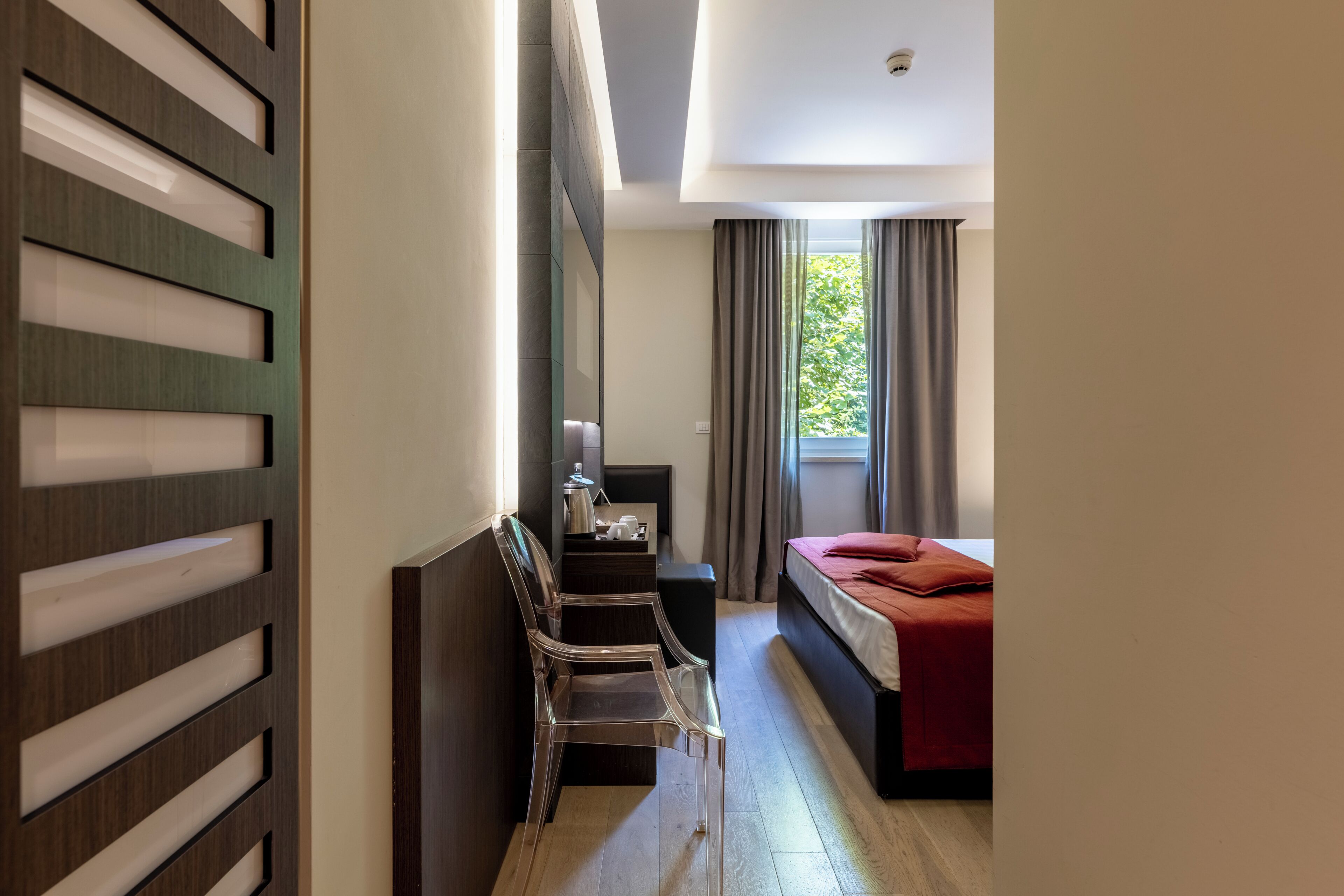 Habitación de hotel con cama, escritorio y silla, ventana con cortinas y pared con diseño decorativo.