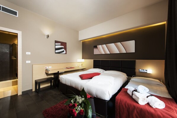 A hotel room with two beds, a bench, a desk, and a wall-mounted TV.