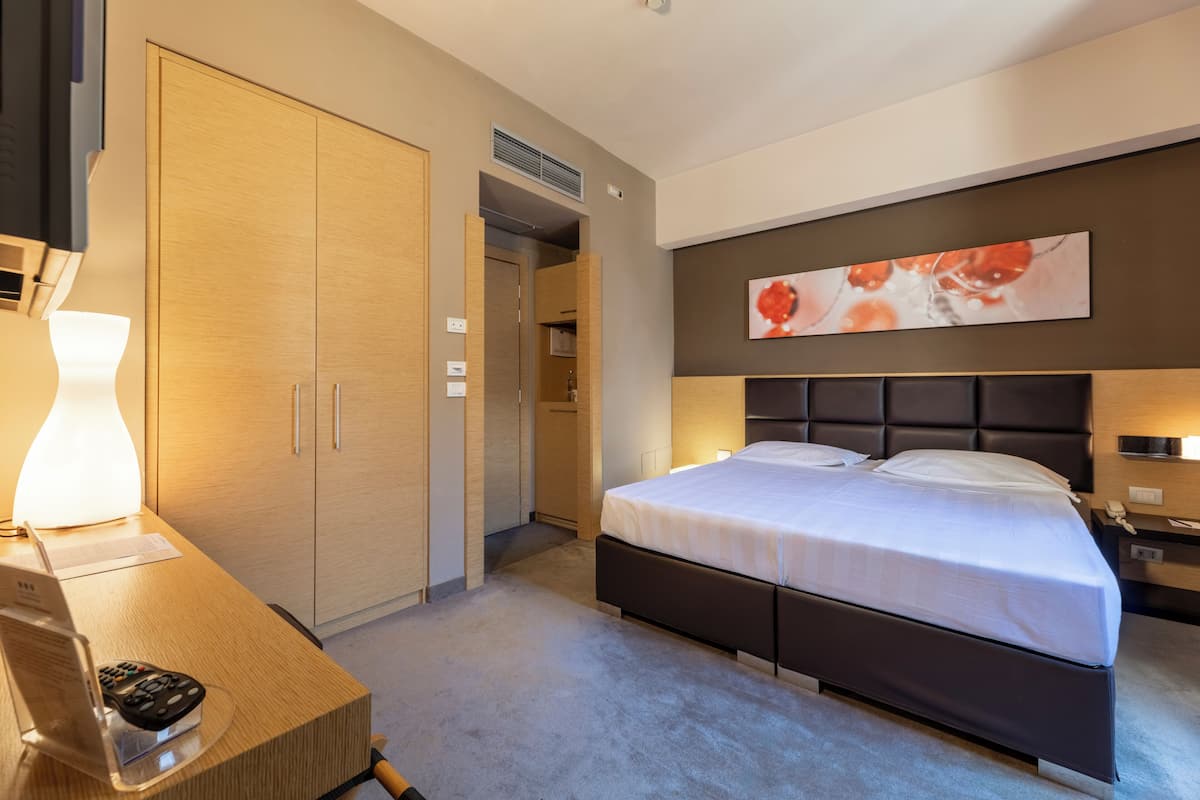 Habitació d'hotel amb un llit, una taula de nit, una làmpada i un quadre a la paret.