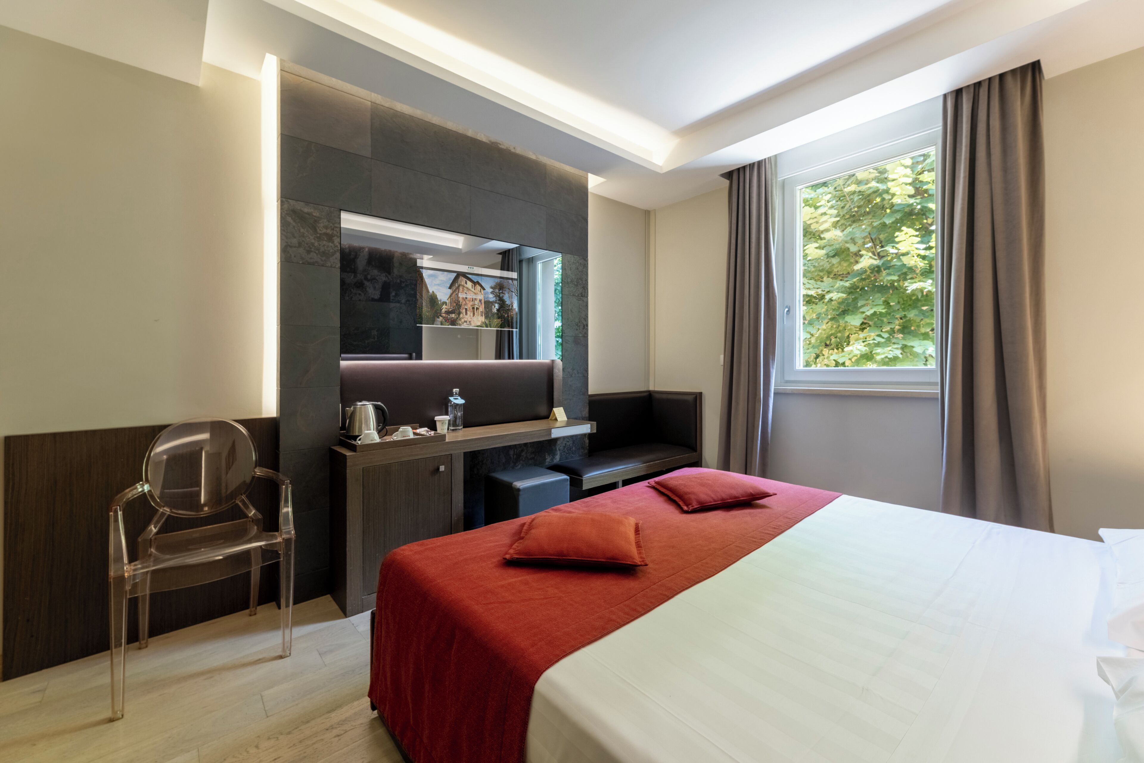 A hotel room with a bed, a desk, a chair, a TV, and a window with curtains.