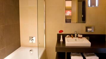 A modern bathroom with a bathtub, a sink, a mirror, and a vase with a red flower.