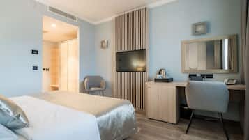 A modern hotel room with a bed, a desk, a chair, a mirror, and a wardrobe.