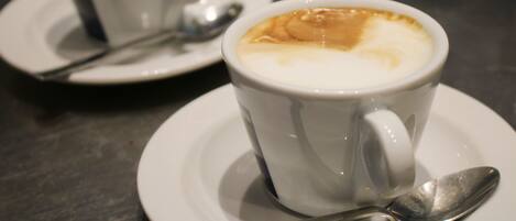 Two white cups of coffee with foam on top, each with a spoon on a saucer.