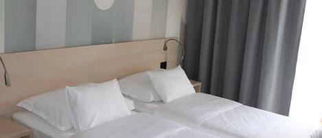 Una cama doble con sábanas blancas en una habitación de hotel.