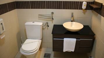 A bathroom with a toilet, sink, towel rack, and a soap dispenser.