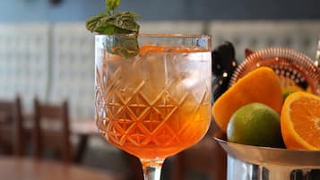A cocktail glass with a mint garnish, a metal bucket with citrus fruits, and a blurred background of a restaurant setting.