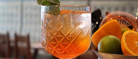A cocktail glass with a mint garnish, a metal bucket with citrus fruits, and a blurred background of a restaurant setting.