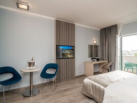 Quarto de hotel moderno com uma cama, uma escrivaninha, duas cadeiras, uma TV e uma varanda com vista.