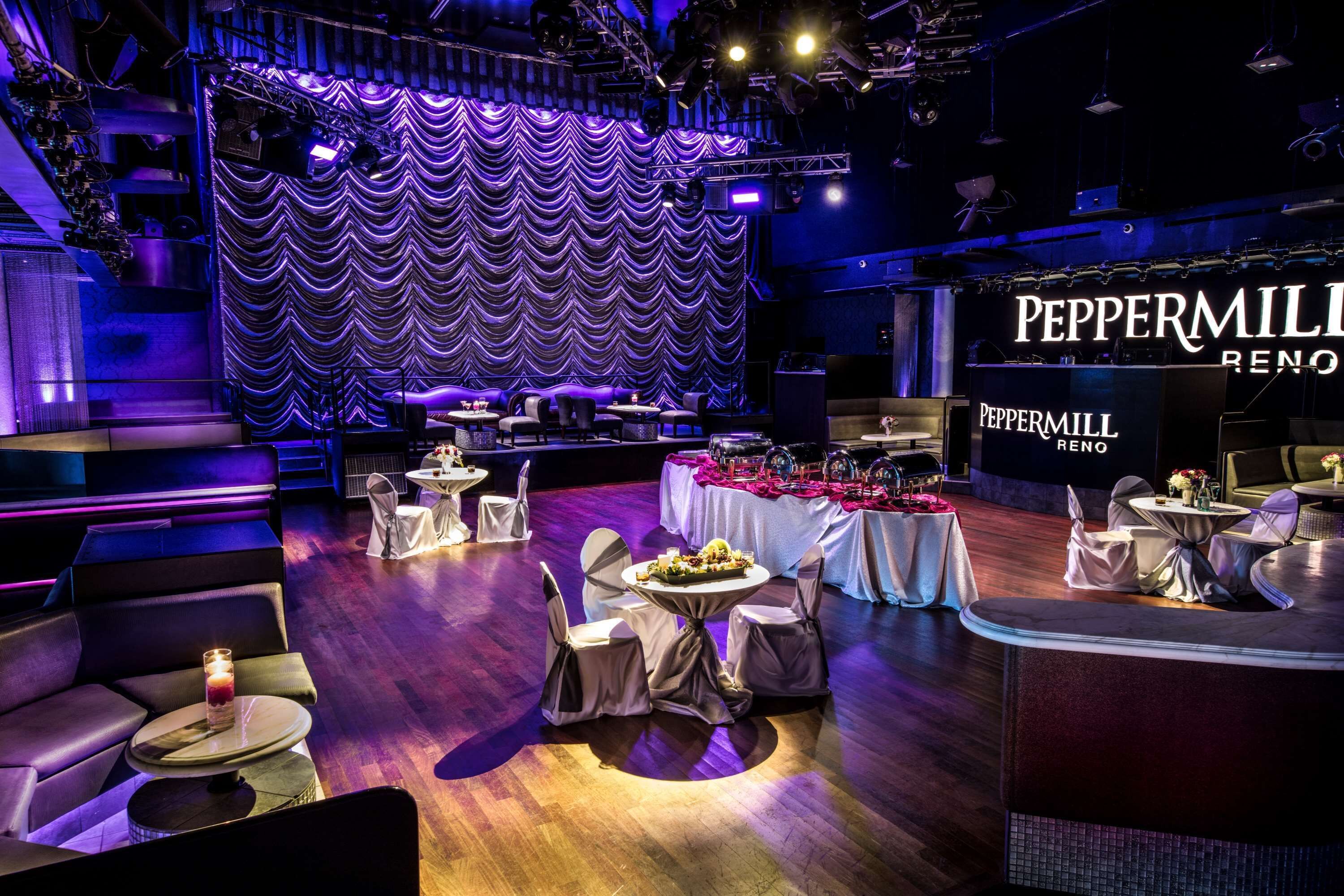 A stage with a wavy curtain backdrop and a sign for 'Peppermill Reno'. Tables with white tablecloths and chairs are arranged in the foreground.