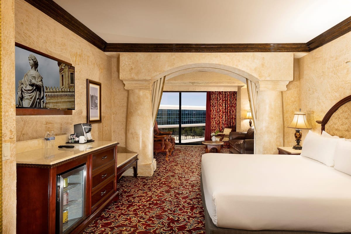 A hotel room with a bed, a desk, a chair, a small table, a coffee machine, a TV, and a large window with a view.