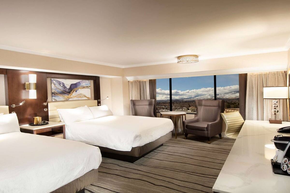 Ein Hotelzimmer mit zwei Betten, einem Schreibtisch, einem Stuhl, einem kleinen Tisch und Bergblick.