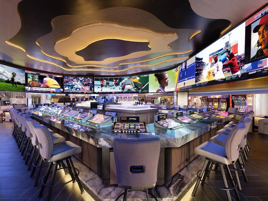 A bar area with multiple screens displaying sports events, a bar counter with stools, and a modern ceiling design.