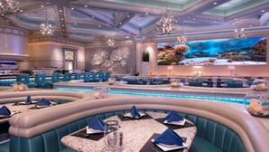 Un restaurant moderne avec des banquettes turquoise, des tables en marbre et un grand mur décoré d’un aquarium.