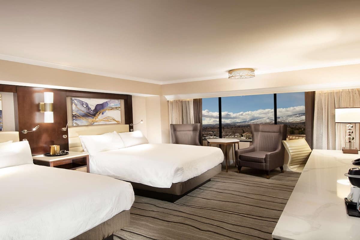A hotel room with two beds, a desk, a chair, a coffee maker, and a view of the mountains.