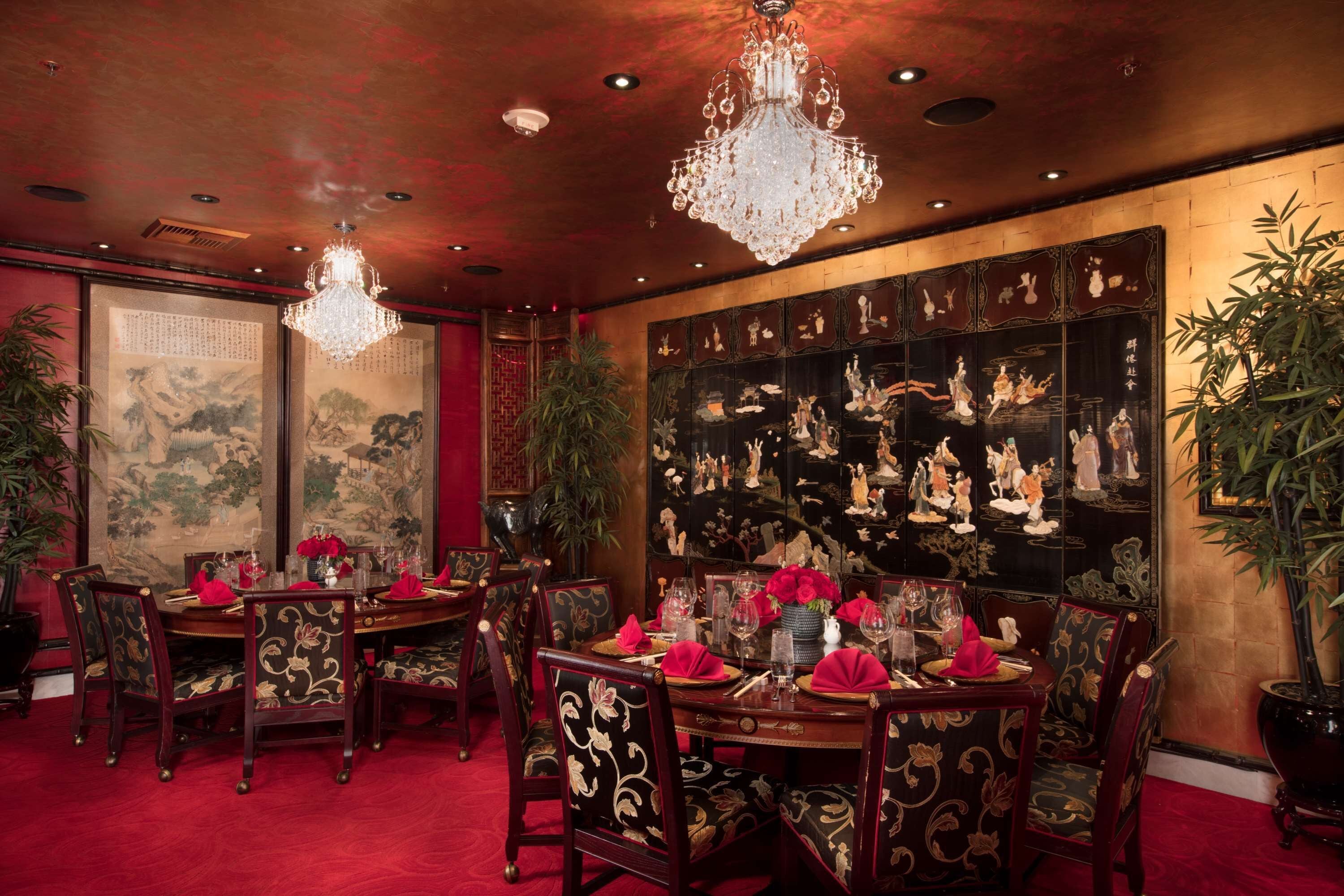 A traditional dining room with ornate wooden furniture, red carpets, and a large wall of decorative art.