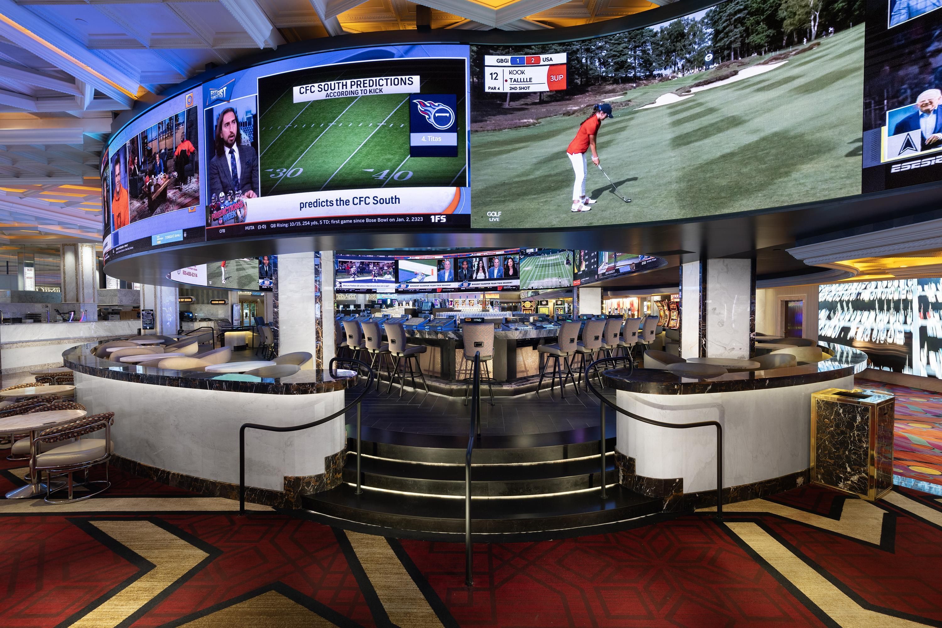 A hotel lobby with multiple screens displaying sports events, a bar area with seating, and a reception desk.