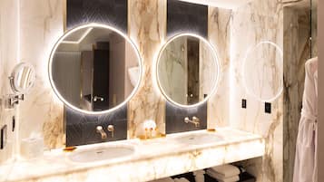 Casa de banho com duas pias, bancadas de mármore e três espelhos redondos com iluminação.