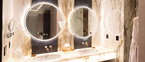 A bathroom with two sinks, marble countertops, and three round mirrors with lights.