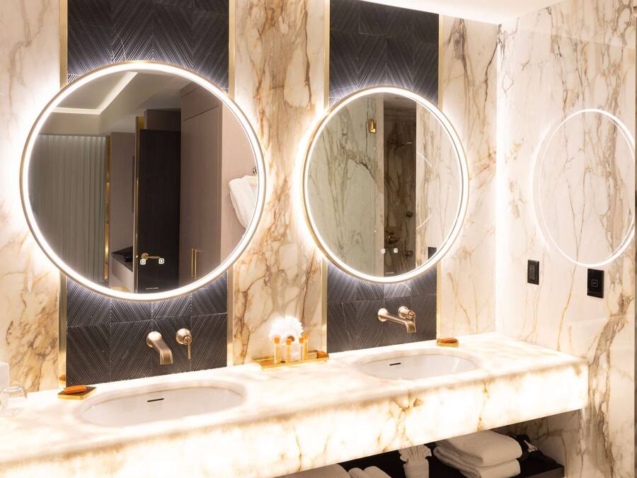 Casa de banho com duas pias, bancadas de mármore e três espelhos redondos com iluminação.