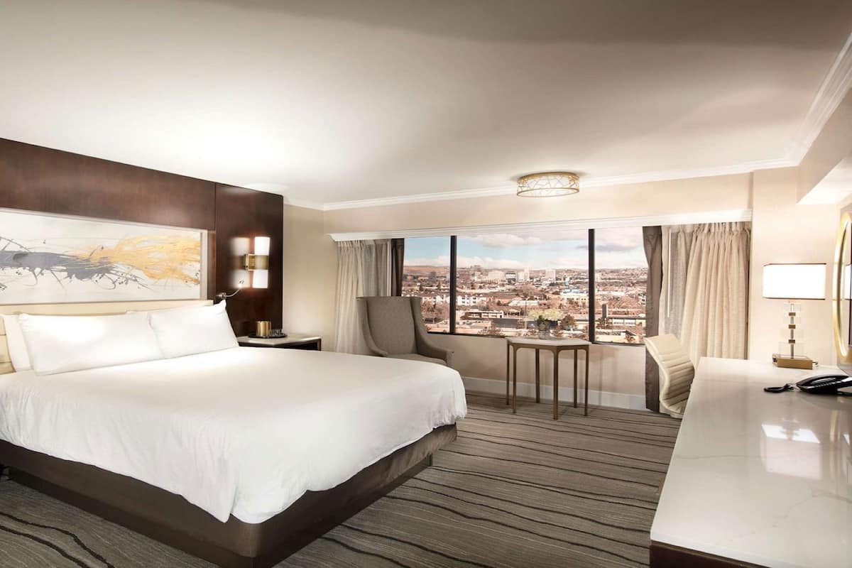 Ein Hotelzimmer mit einem großen Bett, einem Schreibtisch, einem Stuhl, einem kleinen Tisch und Blick auf die Stadt.