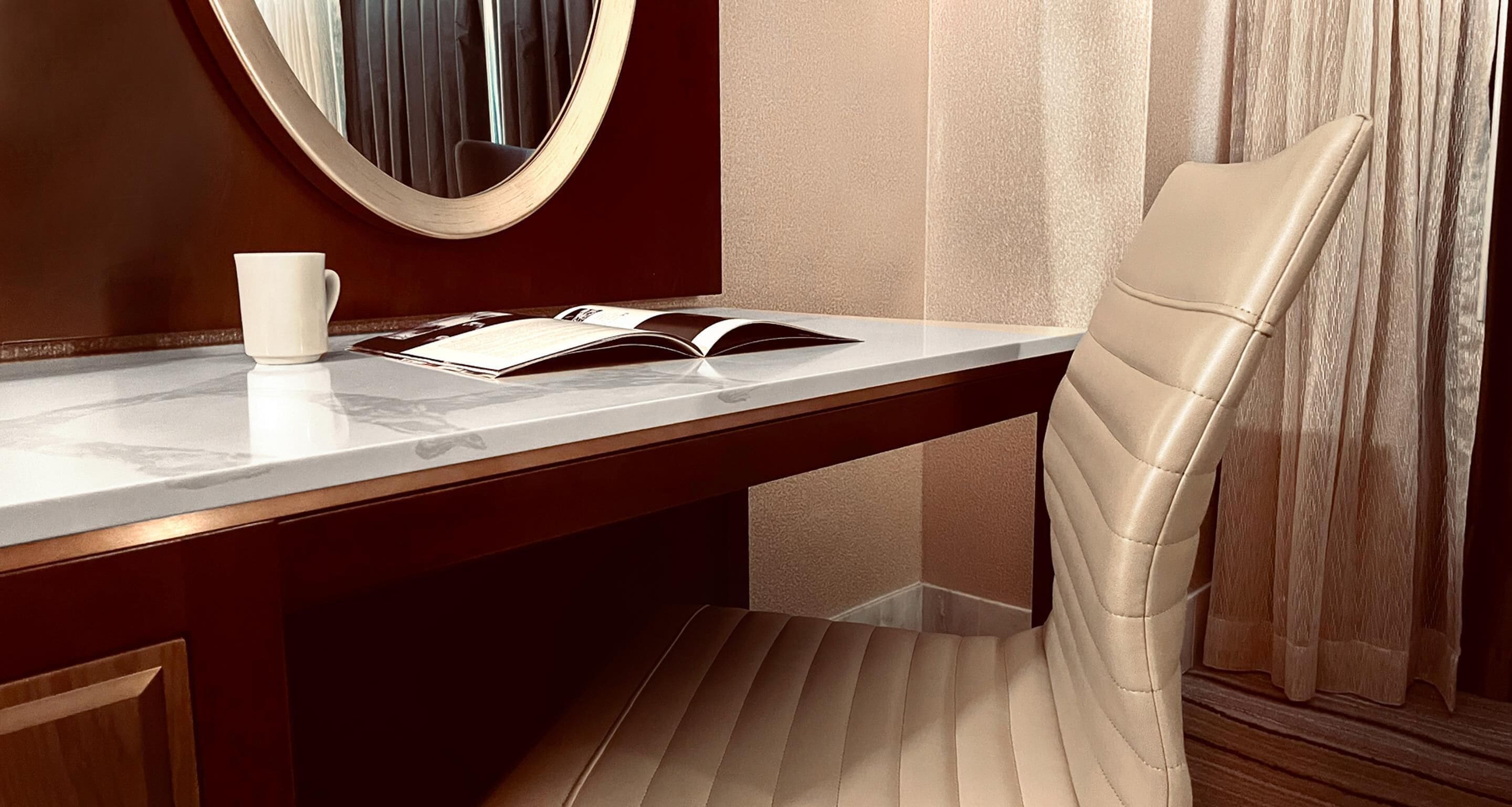 A modern hotel room with a marble desk, a leather chair, a book, and a white cup.