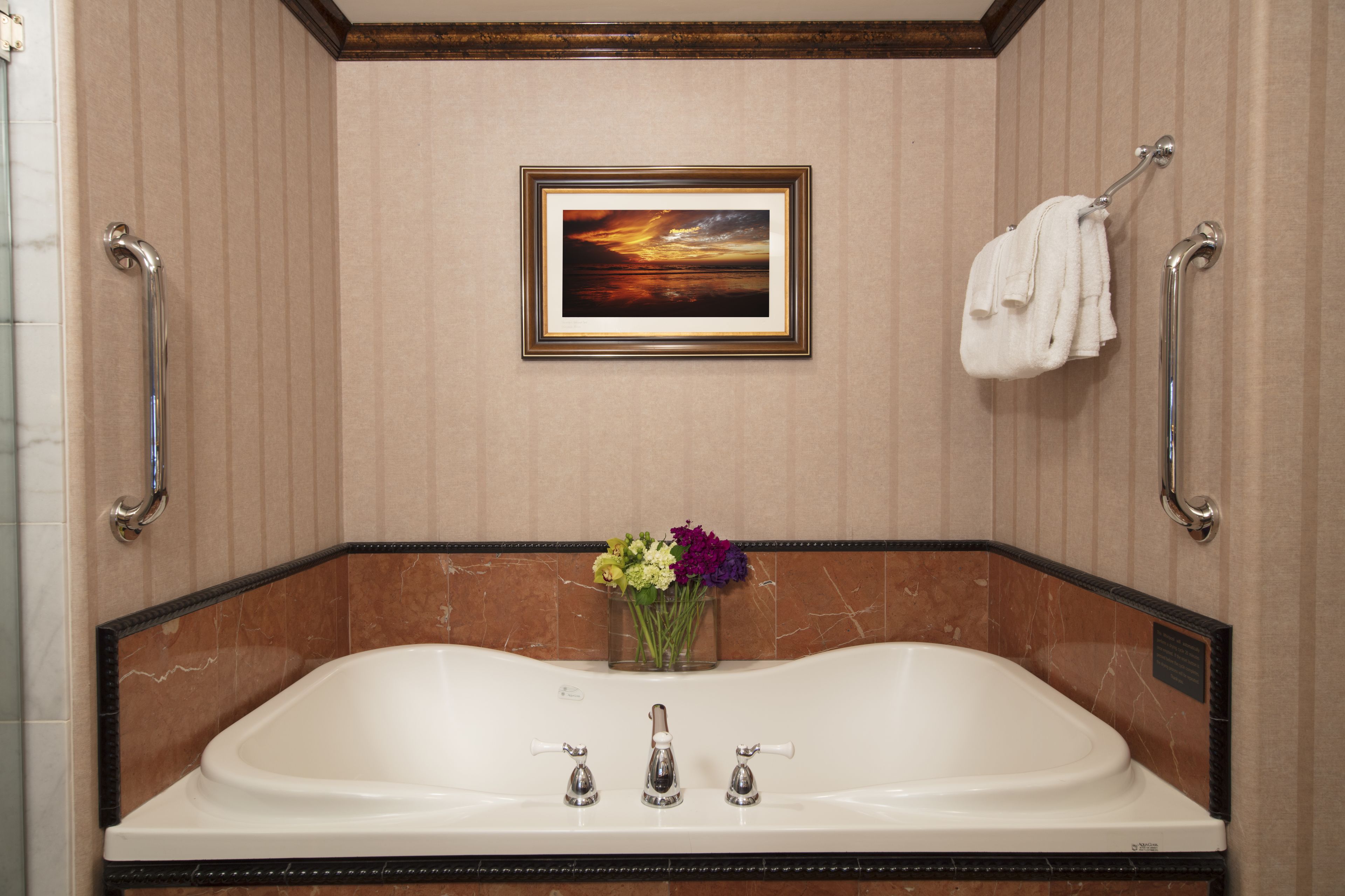 Un baño con una bañera grande, un cuadro en la pared y un florero con flores.