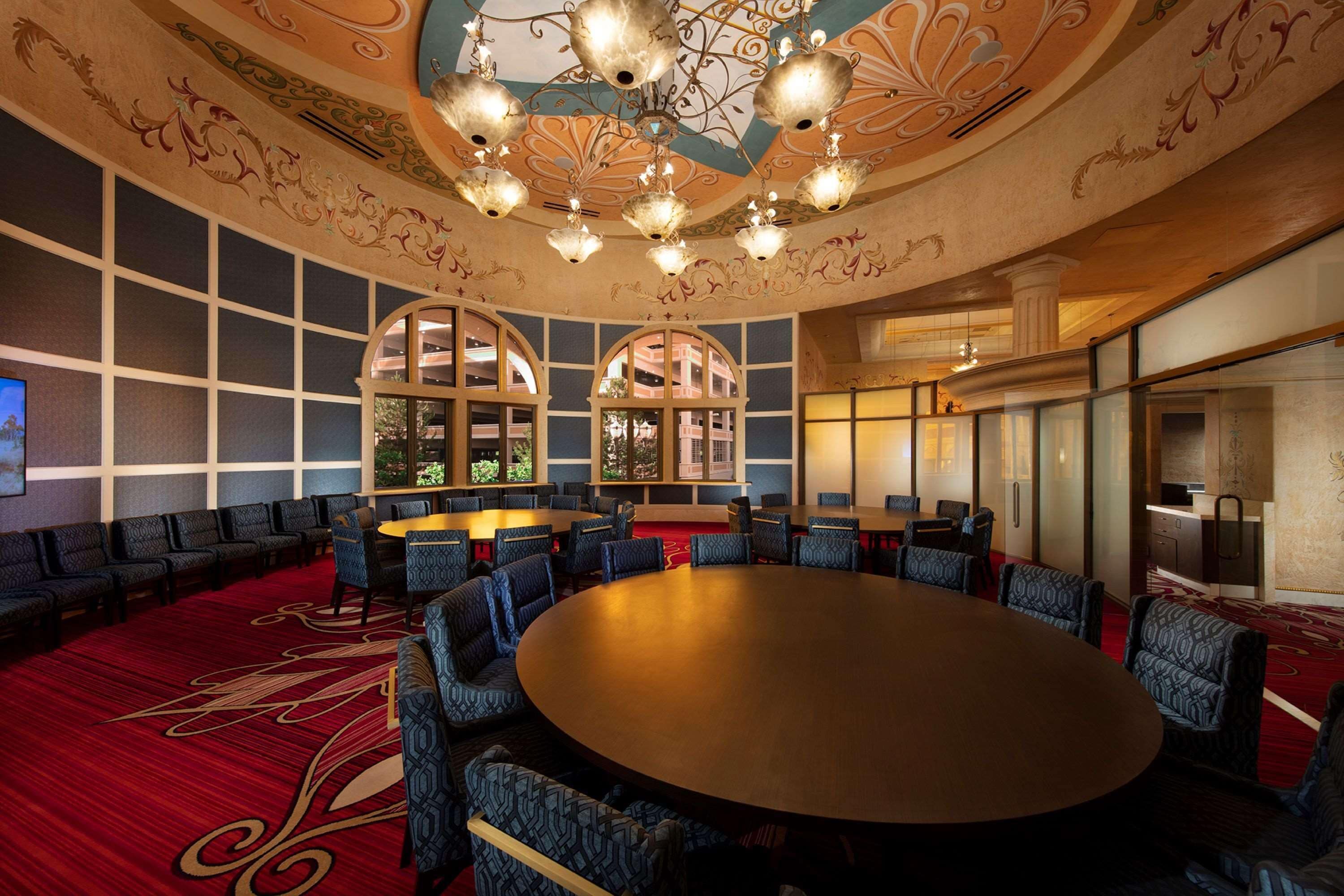 Een vergaderzaal met een grote ronde tafel, blauw gestreepte stoelen en een rood tapijt.