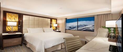 Habitación de hotel con una cama grande, un escritorio, una silla, una mesita de noche, una lámpara y un cuadro de un paisaje montañoso nevado.
