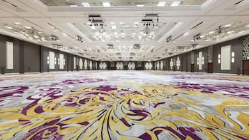 Un salón de conferencias amplio con alfombra estampada, varias luces en el techo y una larga fila de ventanas.