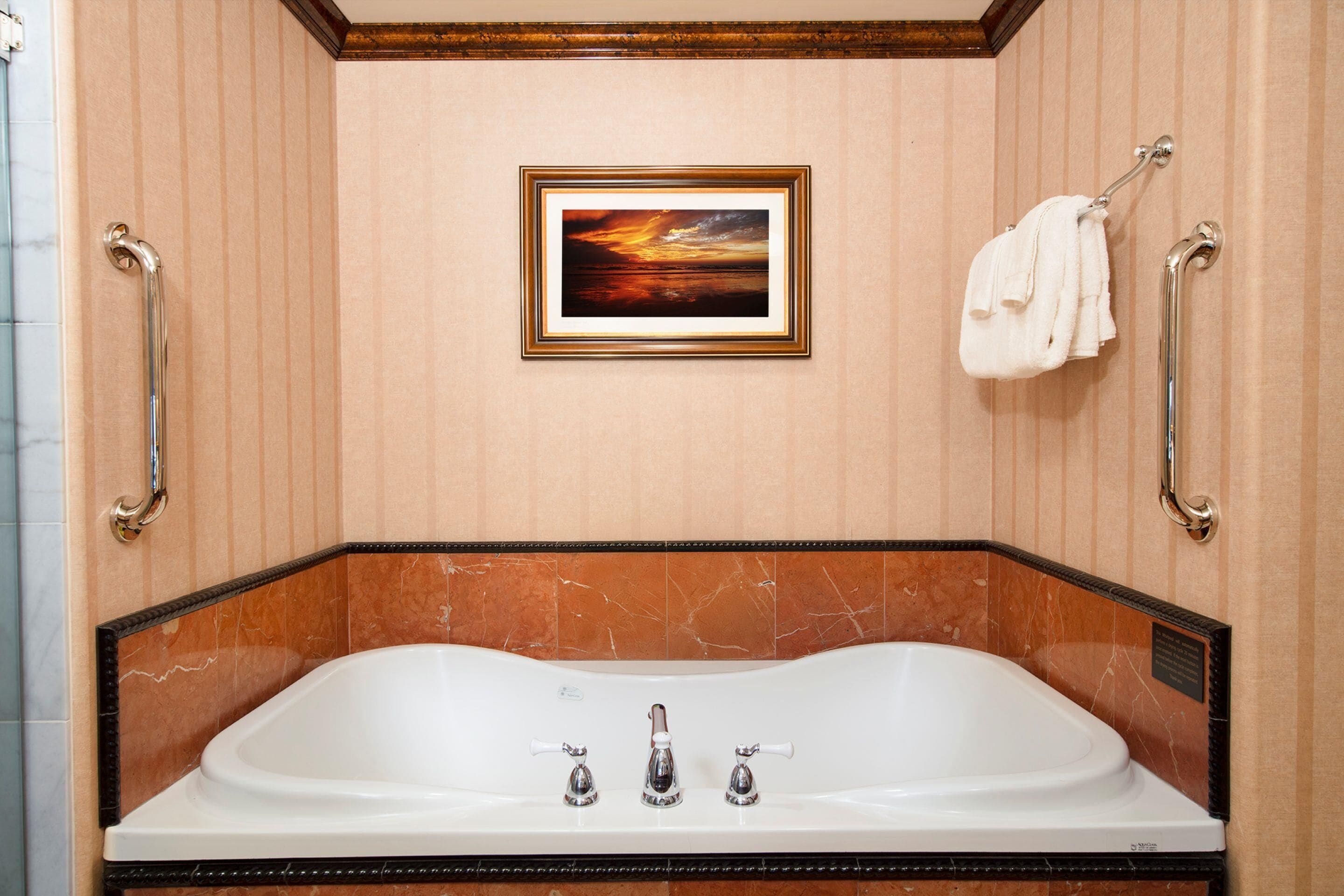 A bathroom with a large bathtub, a framed picture on the wall, and a towel rack.