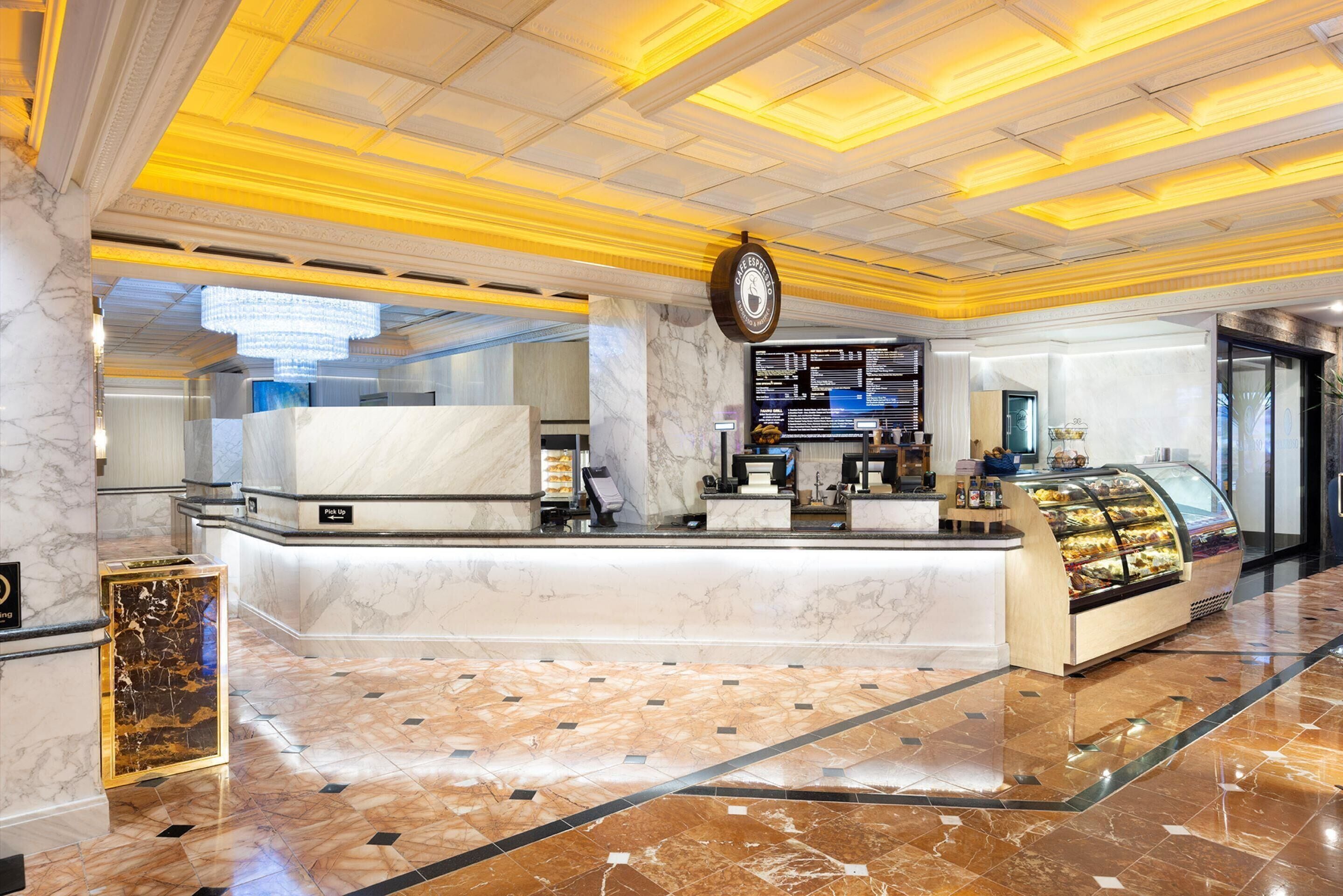 Een hotel lobby met een marmeren receptiebalie, een digitaal menuboard en een vitrine met gebak.