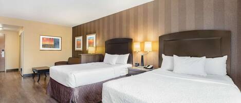 A hotel room with two beds, a desk, and a chair. There are two framed pictures on the wall and a lamp on the desk.