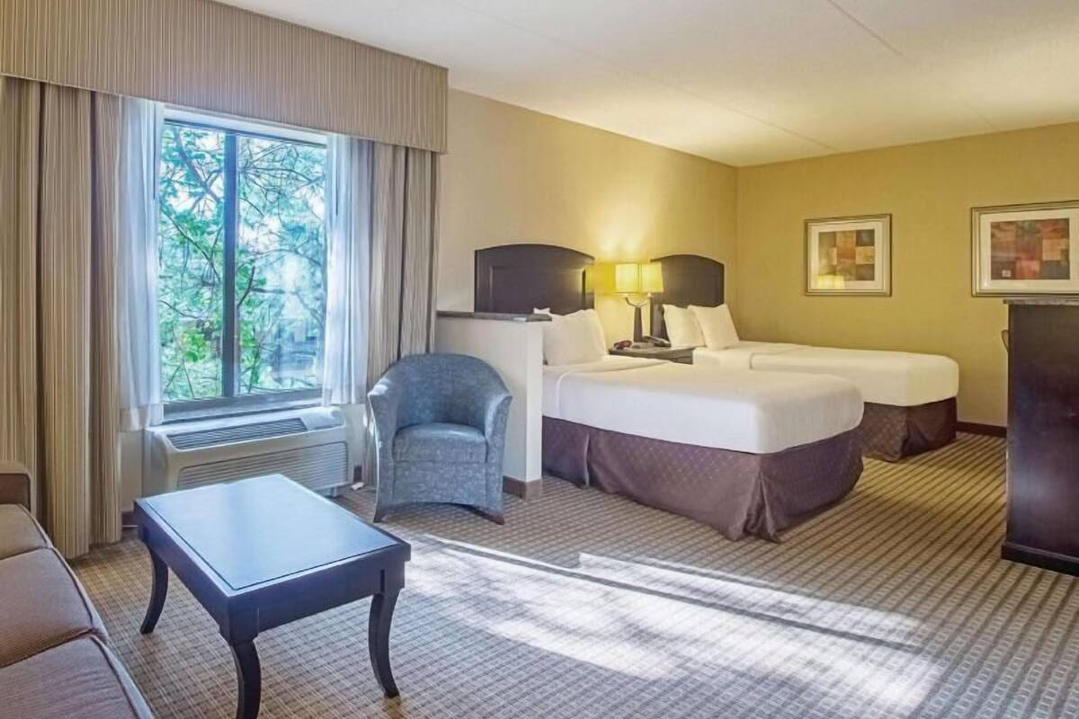 A hotel room with a bed, a chair, a table, and a window with curtains.