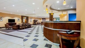 Vestíbulo de hotel con mostrador de recepción, zona de estar y una pantalla grande.