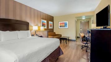 A hotel room with a large bed, a desk with a computer, a chair, a TV, and artwork on the walls.