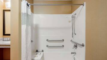 Une douche blanche équipée de barres d’appui, d’un rideau de douche et d’un pommeau de douche amovible.