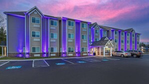 A multi-story hotel with a parking lot, marked handicapped parking spaces, and a building illuminated with purple lights. - Microtel Inn & Suites by Wyndham Manchester (Manchester)