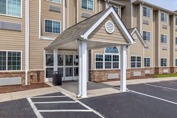 A hotel entrance with a covered waiting area, a brick facade, and a parking lot. - Microtel Inn & Suites by Wyndham Manchester (Manchester)